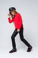 Portrait of beautiful young redhead girl wearing red sweater and black pants posing in studio.