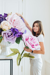 Photo of pleasant looking female florist or gardener makes luxurious bouquet with big roses, decorates hall, works in flower shop, dressed casually. Satisfied brunette woman likes beautiful flowers.