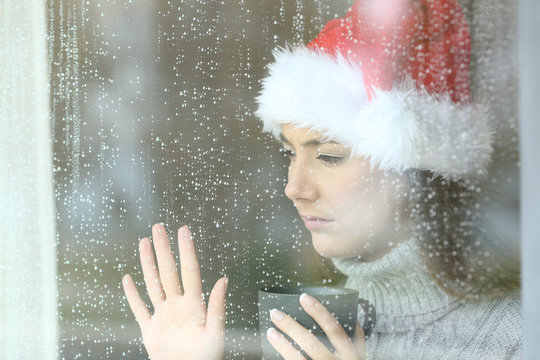Sad woman looking through a window in christmas