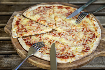 Fresh italian pizza Margherita pizza on wooden chopping board with fork and knife for two, top view