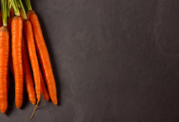Bunch of fresh raw carrots on dark background.