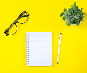 Workspace with notepad and pen on yellow background.