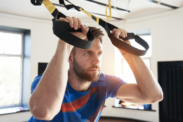 Portrait of handsome man athlete doing exercise alone with fitness belts in modern gym club,...