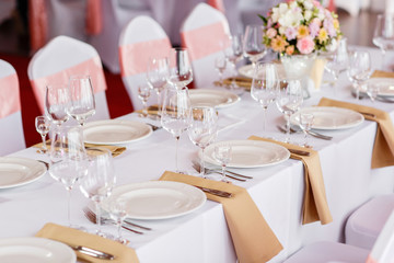 Table at a luxury wedding reception. Beautiful flowers on the table. Serving dishes, glass glasses, waiters work,