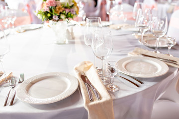 Round table at a luxury wedding reception. Beautiful flowers on the table. Serving dishes, glass glasses, waiters work,