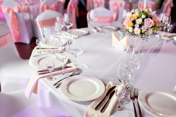 Round table at a luxury wedding reception. Beautiful flowers on the table. Serving dishes, glass glasses, waiters work,