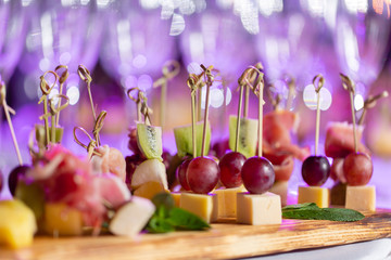 the buffet at the reception. Assortment of canapes on wooden board. Banquet service. catering food, snacks with cheese, jamon, prosciutto and fruit