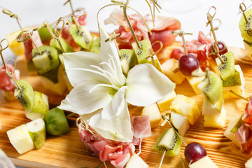 the buffet at the reception. Assortment of canapes on wooden board. Banquet service. catering food, snacks with cheese, jamon, prosciutto and fruit