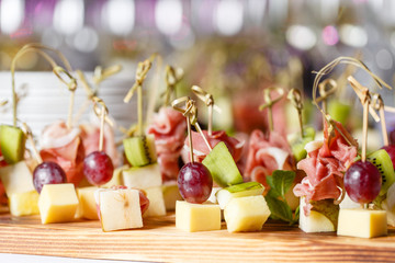 the buffet at the reception. Assortment of canapes on wooden board. Banquet service. catering food, snacks with cheese, jamon, prosciutto and fruit