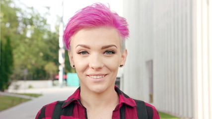 A happy smiling woman with a pink hair in the city street. Close-up shot. Soft focus