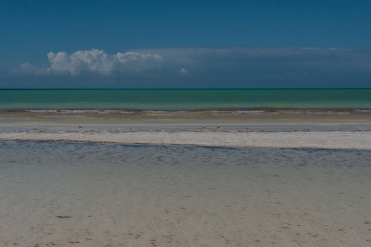 Stripes of white shallow water, white sand, and aqua seas under a deep blue sky with a dramatic line of clouds over the horizon paint a picture of a tropical paradise on Isla Holbox, Mexico.
