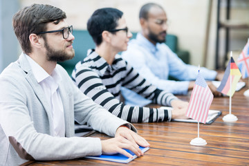 Serious confident consuls of different countries attentively listening to speaker and sitting in...