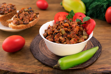 A serving of vegetable stew with a bitter pepper and tomatoes, a wooden background.
