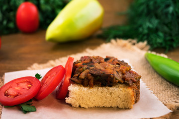 Stewed chopped vegetables on a piece of white bread next to tomato slices on a paper napkin.