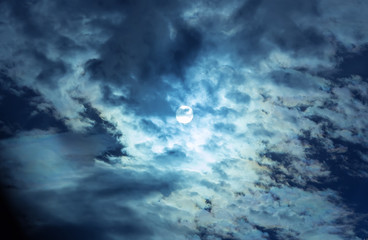 The full moon in the night sky hiding behind the clouds.