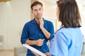 Waist up portrait of mature man explaining symptoms to nurse standing in hall of modern dental clinic, copy space