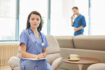 Fototapeta premium Portrait of female doctor posing in office of modern clinic holding clipboard, copy space