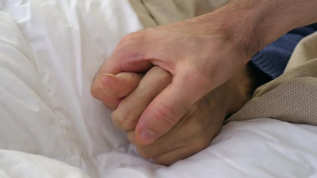 Close-up of a young man holding his grandmother's hand. 4K footage
