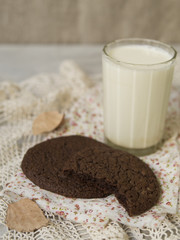 Autumn theme background. Chocolate cookies with a glass of milk, dry autumn leaves on gray background with lace napkin. Copy space, selective focus