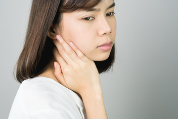 Asian girl in white casual dress catch that shoulder, Because of the pain of hard work. Or something hit the shoulder. on a gray background gives a soft light.