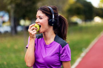 Beautiful fit woman eating green apple after training