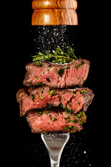 Sliced beef steak from grill on a fork. Salt is strewing from wooden mill - obrazy, fototapety, plakaty