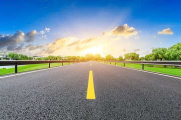 Empty asphalt road and green forest with colorful clouds at sunset