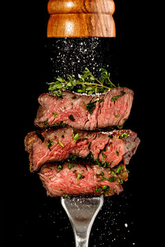 Sliced beef steak from grill on a fork. Salt is strewing from wooden mill