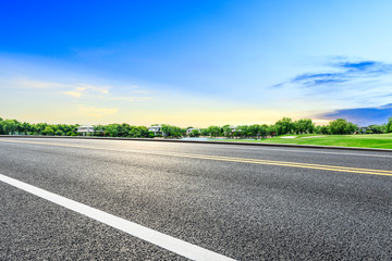Empty asphalt road and green forest with colorful clouds at sunset