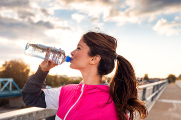 Side view of fitness woman drinking water at sunset