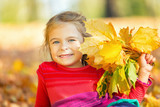 Happy little girl with autumn leaves in the park