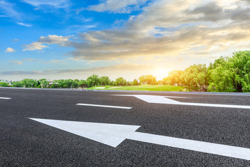 Empty asphalt road and green forest with colorful clouds at sunset