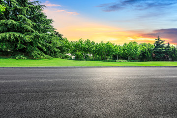Empty asphalt road and green forest with colorful clouds at sunset