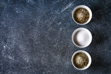 Obraz na płótnie Canvas Different types of salt in glass bowls on a dark gray table.