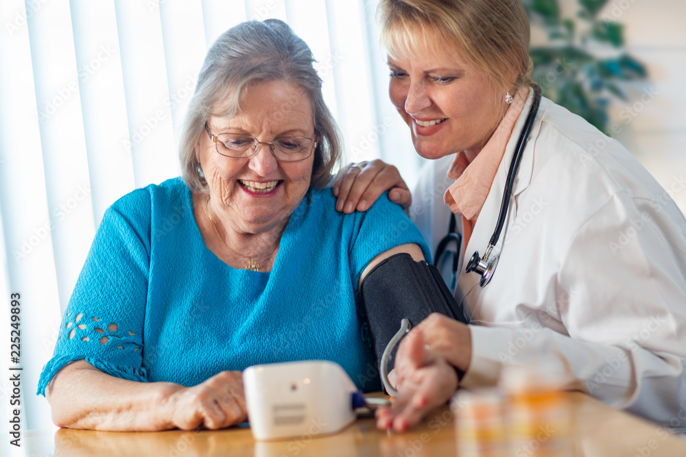 Wall mural senior adult woman learning from female doctor to use blood pressure machine