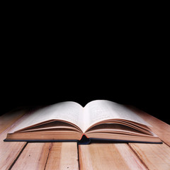 Opened Book on Wooden Table Against Black Background