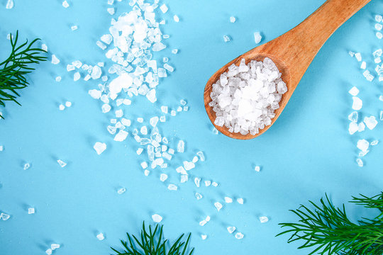 Crystals of large sea salt in a wooden spoon and dill on a blue table.