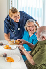 Fototapeta na wymiar Female Doctor or Nurse Serving Senior Adult Couple Sandwiches at Table