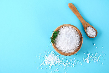Crystals of large sea salt in a wooden bowl and spoon and dill on a blue table.