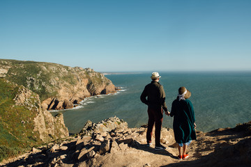 Young couple in hats standing at the cliff and watching the sea. Cabo da Roca, Portugal