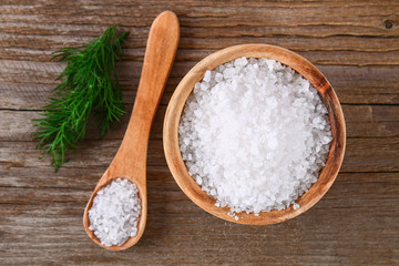 Fototapeta na wymiar Crystals of large sea salt in a wooden bowl and spoon and dill on a table.