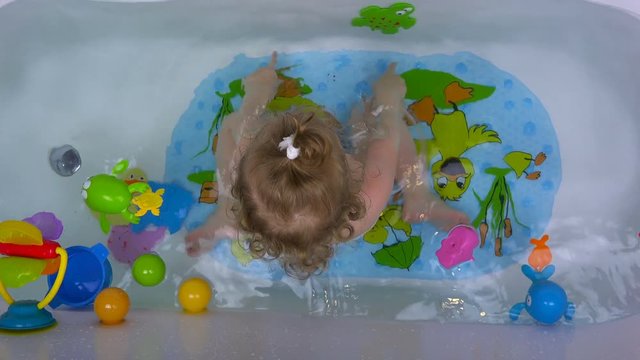 a two-year-old girl in the bathroom splashing with water. View from above.