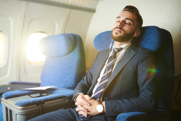 Portrait of handsome bearded businessman wearing earphones sleeping blissfully while enjoying first class flight in plane, copy space - Powered by Adobe