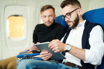Portrait of handsome bearded man using digital tablet while enjoying first class flight in plane, copy space