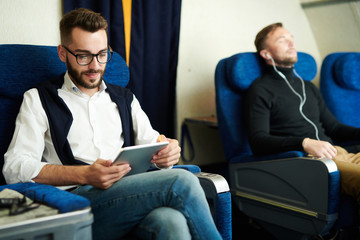 Portrait of two handsome men enjoying first class flight in comfortable seats of modern plane, copy space