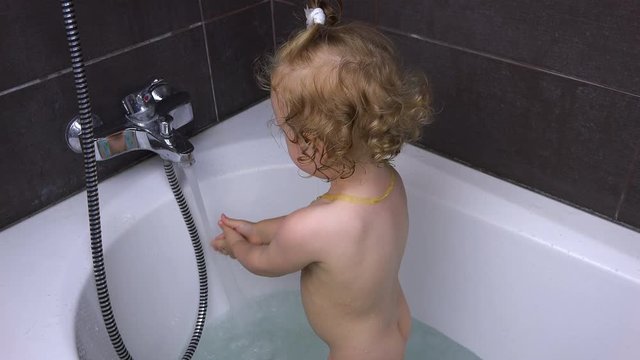 the girl turns on a mixer with water, adding water to the bath.
