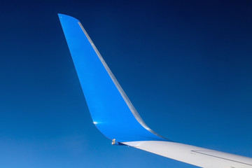 The blue winglet on a wing of plane when a flight in a blue sky. Part of jet wing, close view.