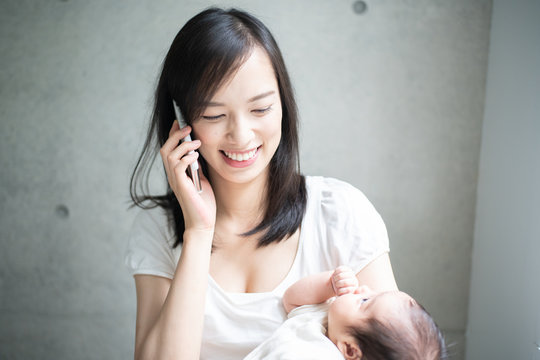 赤ちゃんを抱きながら携帯電話で話す女性
