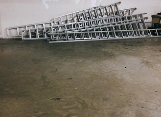 Multiple long metal ladders stacked together on the ground