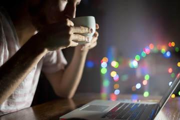 night time worker in office sitting at the table using laptop and drink coffee  f